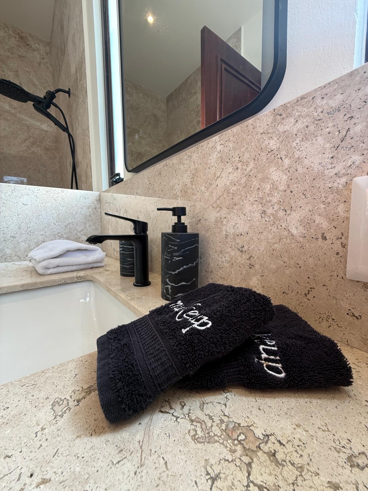 Travertine bath vanity with plush towels and black fixtures