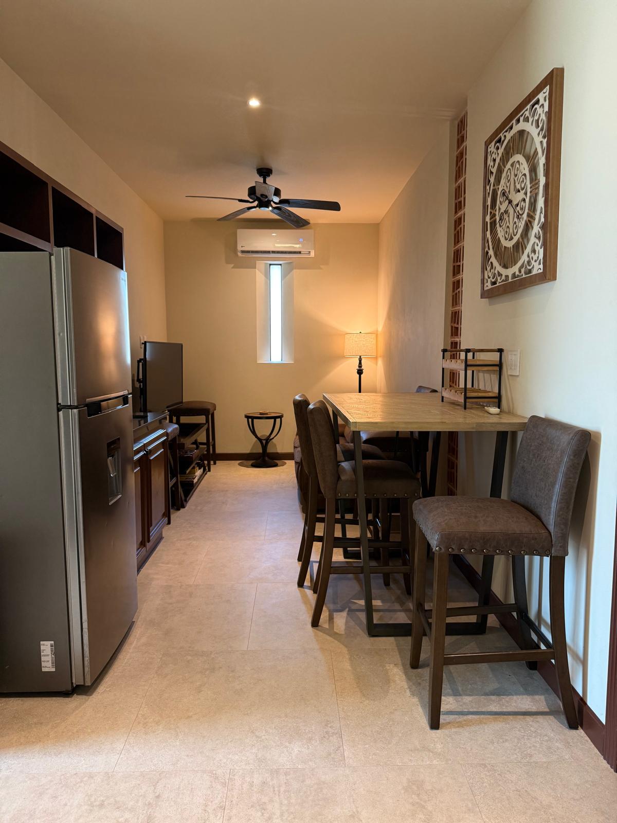 Suite kitchenette with refrigerator, high-top dining table, and ornate wall clock