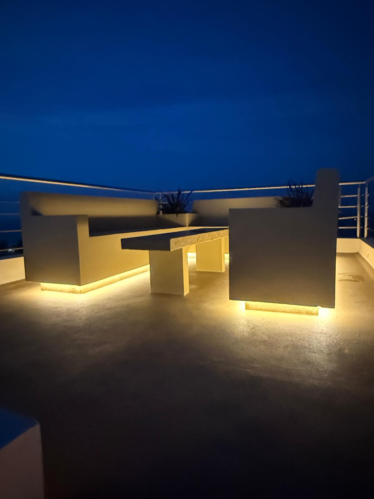 Illuminated rooftop terrace bench and stone table at blue hour