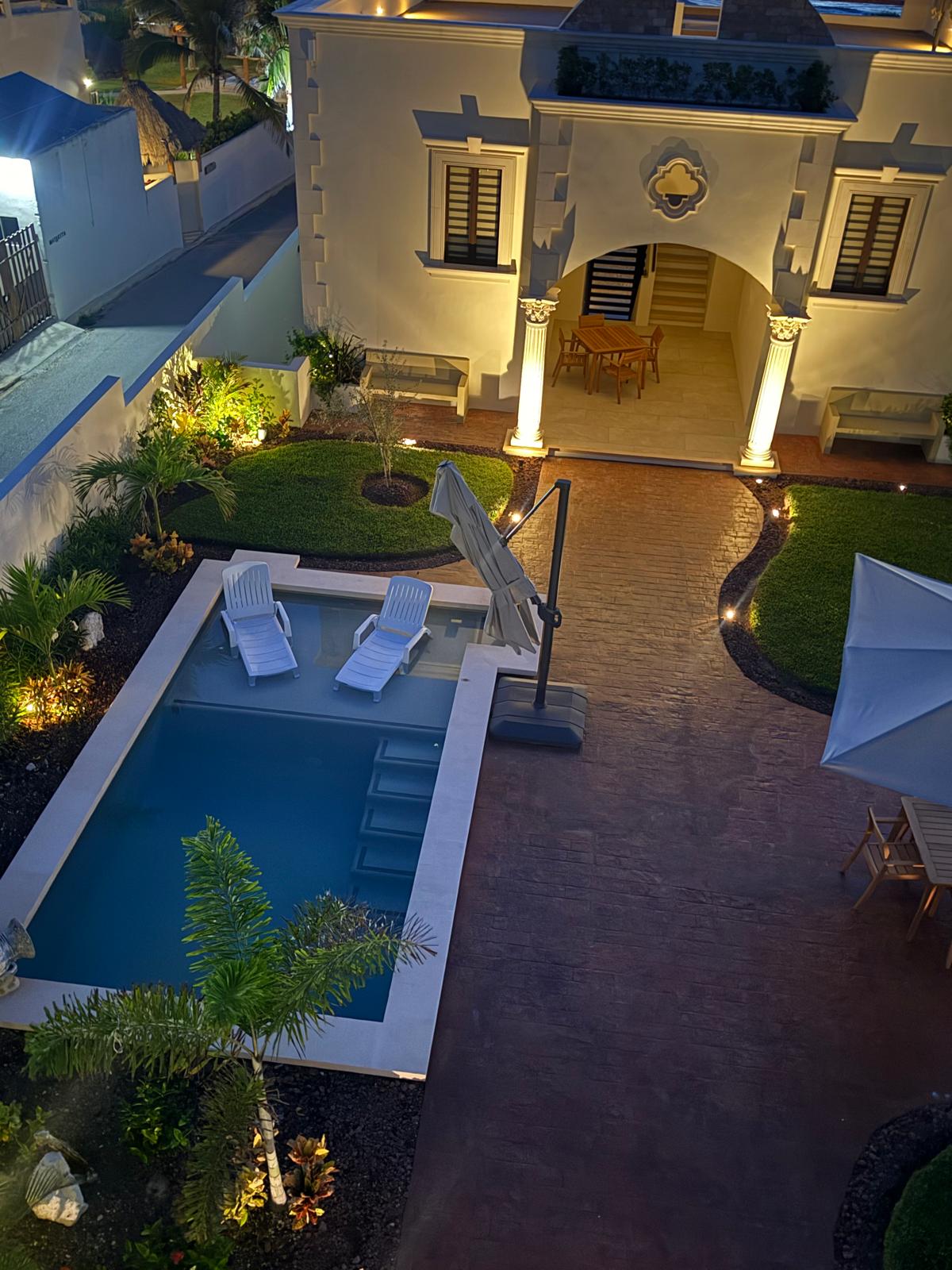 Illuminated courtyard pool, loungers, and arched loggia from above at dusk